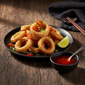 Asian Fried Calamari on a dark ceramic plate with crispy golden rings and tentacles, garnished with red chilies, spring onions and sesame seeds, served with sweet chili dipping sauce
