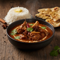 Goat Curry in a dark ceramic bowl with rich deep brown sauce and tender goat meat pieces, garnished with cilantro and whole spices, served with basmati rice and naan